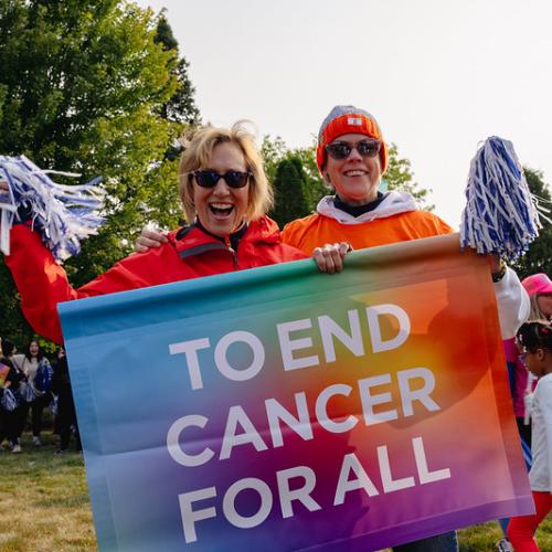 two women holding sign that says to end cancer for all